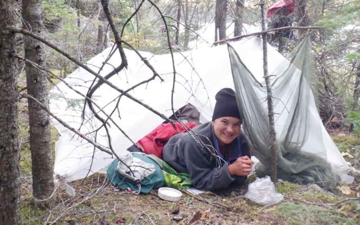 a person smiles from under a tarp shelter amongst trees